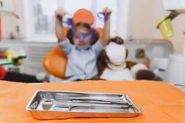 Metal tray with clean dentist instruments placed on table on blurred background of little patient in modern clinic