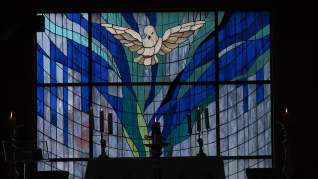 stained glass with figure of the holy spirit and candle or paschal candle