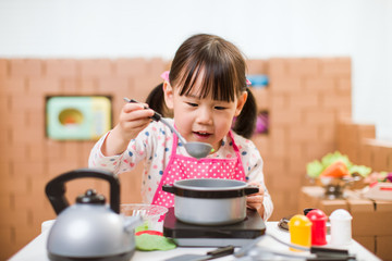 toddler girl pretend play food preparing role against cardboard blocks kitchen background