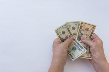 Top view close-up of the hands of an old woman counts money US dollars on a white table background.