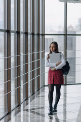 attractive girl walks in a bright corridor with laptop and things in airport terminal or office. travel atmosphere or alternative work atmosphere. freelancer student travels to business meeting.