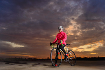 Fototapeta na wymiar Portrait of Young Woman Cyclist with Road Bike at Sunset. Healthy Lifestyle and Outdoor Sport Concept