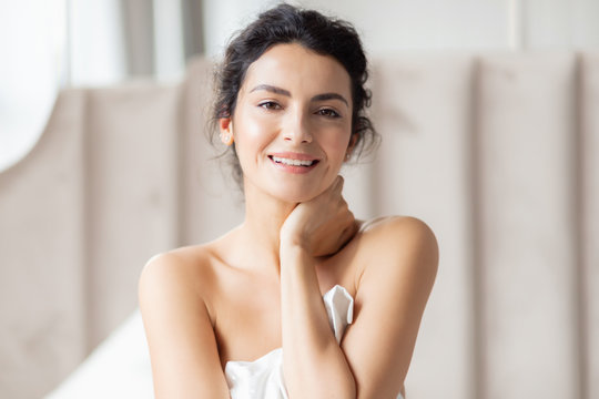 Smiley brunette woman looking at camera and embracing white pillow.