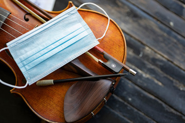 A face mask on an acoustic violin or viola with a pencil and a bow next to it representing...