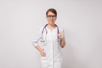 A young beautiful female doctor holds a stethoscope on an isolated white background. The concept of a European doctor