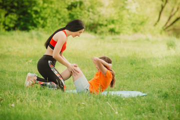 Fitness coach helps girl completing the exercise. Make sports open air. Healthy lifestyle concept. Baby yoga, fitness training. Soft focus