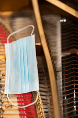 A face mask lying on the strings of a piano representing performance restrictions during a pandemic