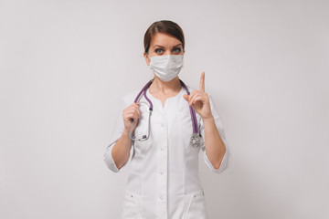 woman doctor in a medical mask in a white coat. Concept female hands show attention sign.