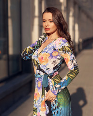 Elegant woman wearing long colorful evening dress and walking city street at sunset light. Pretty...