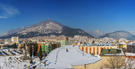 A snowy panoramic view of Sliven, a mountain town in Bulgaria in winter. The Blue Rocks ("Sinite Kamani") mountain in the background.