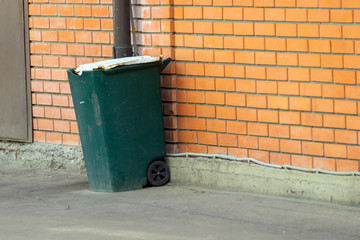 Obraz premium green trash can on wheels near a brick wall