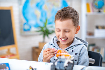 cute seven-year-old boy, schoolboy, has fun with constructor, sitting at table
