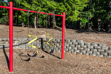 Closed playground swing set on a sunny day, closed and taped off due to Covid 19
