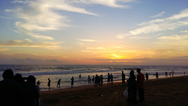 A silhouette landscape image of people watching sunset on a beach in Kerala, India.