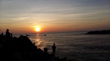 Fototapeta premium A silhouette landscape image of people watching sunset on a beach with fishing boats in Kerala, India.