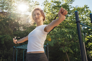 A woman in grey leggings and a white top looks to the side and performs an exercise hand frame to waist the sun's glare from behind