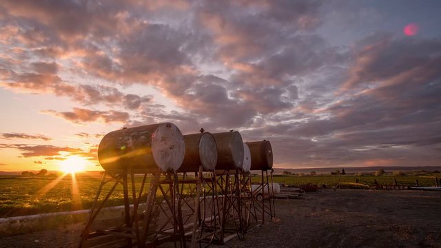 Time lapse of colorful sunset on farm in Southern Idaho with fuel tanks in view as the sky changes color.