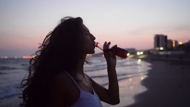 Woman drinking soda on beach with city lights in background
