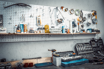 Moto workshop with hand tools. Workbench with sets of keys, screwdrivers, ploskobets, electrical tape, duct tape on the wall. Table with motorcycle parts, vise. Workspace for a joiner, auto mechanic