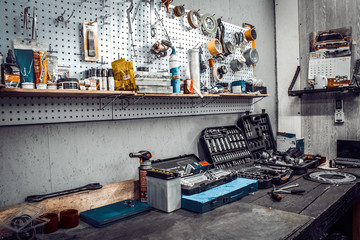 Inside the workshop. Large workbench and tools for working on the table close-up. Workspace for mechanic with wrenches, pliers on a metal wall. Garage for motorcycle repair, car service station.