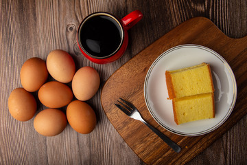 Plate with delicious sliced butter cake with cup of coffee and fresh egg on wooden background.