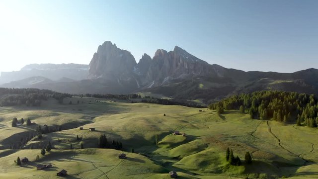Flying backwards above Alpe di Suisi blooming fields meadow in Dolomites Italy Alps. Morning at Seiser Alm mountain valley in South Tyrol