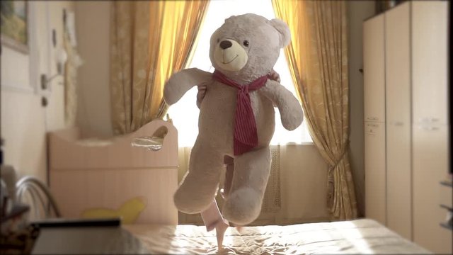 Teddy bear and girl rejoices by jumping on the bed and cheerfully fall down. Girl 8 years European appearance