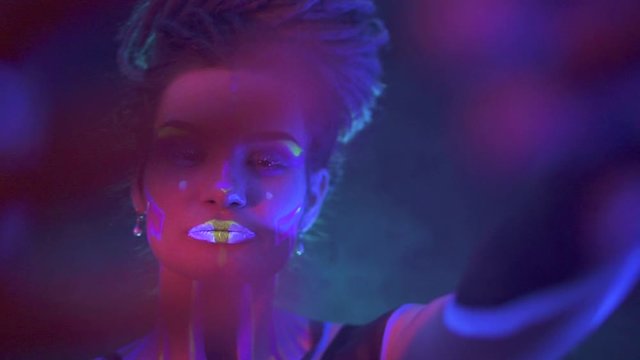 Portrait of a Girl with Dreadlocks in Neon UF Light. Model Girl with Fluorescent Creative Psychedelic MakeUp, Art Design of Female Disco Dancer Model in UV, Colorful Abstract Make-Up. Dancing Lady