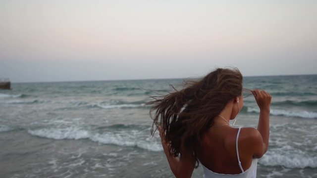 Woman listening to music and dancing on beach after sunset
