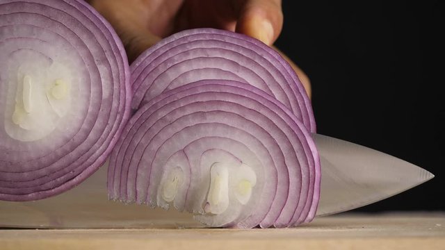 Chef's hand slices fresh shallot on a wooden chopping board on the kitchen table to cook for customers.