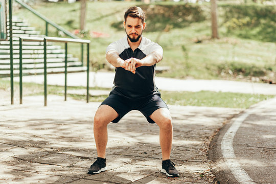 Man wearing sportswear doing squats in public park.