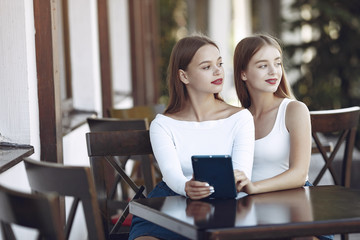 Beautiful girls in a jeans skirts. Women in a summer cafe. Friends using a tablet