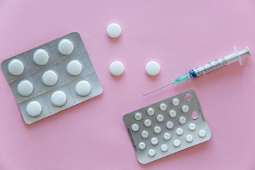 Packages with tablets and syringe on a pink background