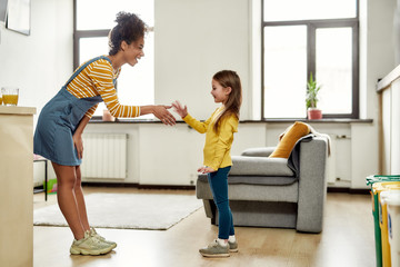Nice to meet you. African american woman baby sitter get acquainted with caucasian cute little girl. They are standing indoors and talking