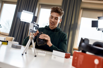 Dream. Create. Record. Young cheerful male technology blogger smiling while recording video blog or vlog about new camera lens at home studio. Blogging, Work from Home concept