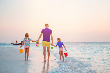 Happy father and his adorable little daughters at tropical beach having fun
