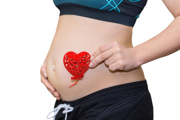 Close up on pregnant belly. Woman expecting a baby holding a red heart with love