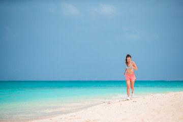 Fototapeta na wymiar Fit young woman doing exercises on tropical white beach in her sportswear