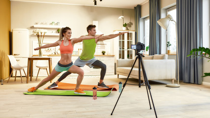 Obraz premium Making Things Done. Full length shot of young couple in sportswear recording video blog or vlog about healthy lifestyle on camera while doing yoga at home. Fitness, workout and vlogging concept