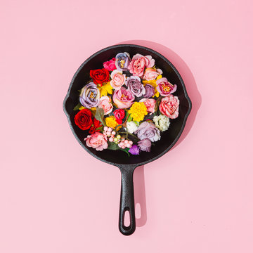 Creative Concept With Spring Flowers And Green Leaves In Frying Pan On Pastel Pink Background. MInimal Nature Flat Lay.