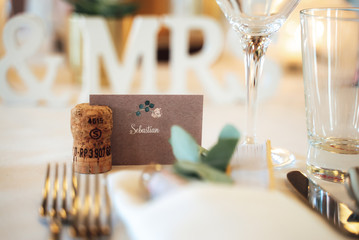 Closeup of label with name of guest in cork stand. Blurred elegant wedding table setting. Wedding day concept.