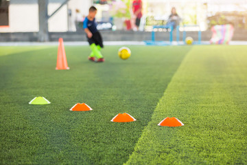 Obraz premium selective focus to marker cones are soccer training equipment on green artificial turf with blurry kid players training background. material for training class of football academy.