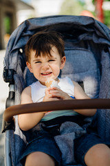 Happy toddler eating ice cream.Messy child eats frozen sweet cone.Kid eating sugar and sweets.Baby diet and unhealthy nutrition.Sugar rush.Excited joyful boy in a stroller.Toothache and tooth decay