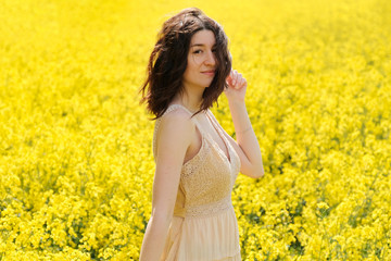 Naklejka na ściany i meble Happy young woman in field with yellow flowers on sunny summer day, closeup portrait. Pretty caucasian model girl with curly hair posing outdoor.