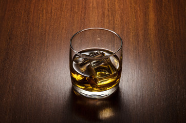 Glass of whiskey on the rocks, positioned on the center of the composition, isolated on wooden background