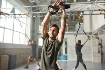 Too fit to quit. Cheerful athletic man doing fitness TRX training exercises at industrial gym