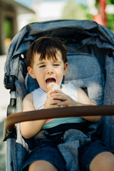 Happy toddler eating ice cream.Messy child eats frozen sweet cone.Kid eating sugar and sweets.Baby diet and unhealthy nutrition.Sugar rush.Excited joyful boy in a stroller