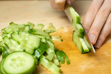 Women's hands cut a fresh cucumber into sticks on a wooden Board close up