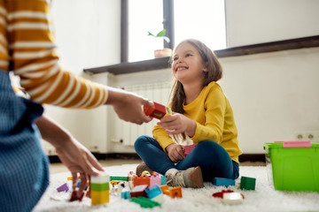 Fun and play all day. Caucasian little girl spending time with african american baby sitter, playing with construction toys set, sitting on the floor