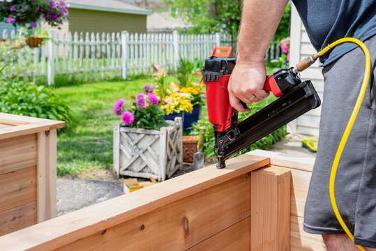 Closeup Of A Man Using A Power Nail Gun To Build Raised Garden Beds